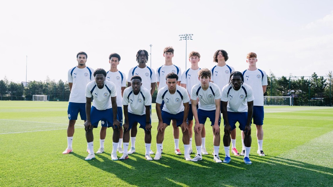 A group photo of eleven young soccer players in Manchester City training kits on a grassy field.